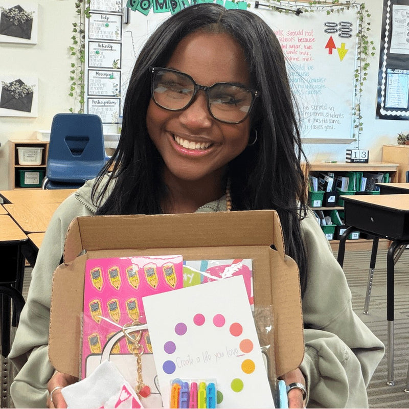 A smiling teacher holding her Teacher Care Crate in her classroom